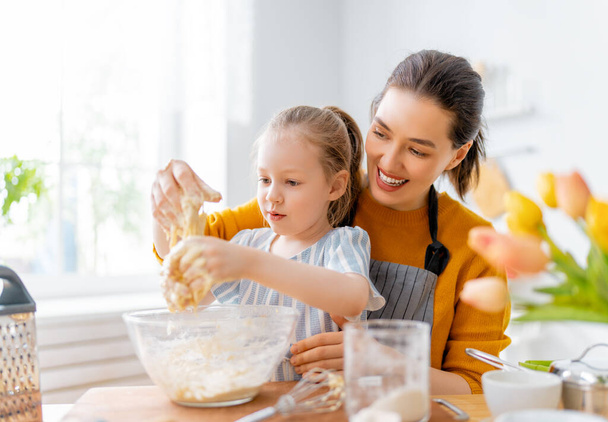 Happy loving family are preparing bakery together. Mother and child daughter girl are cooking cookies and having fun in the kitchen. Homemade food and little helper.     - Photo, Image