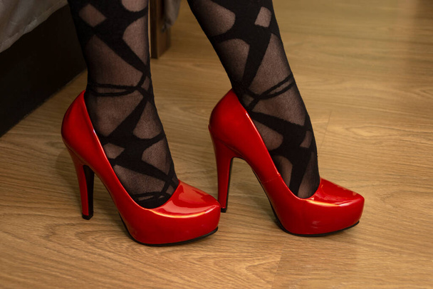 Ноги жінки в червоних туфлях на високих підборах і чорних колготках з візерунком
 - Фото, зображення