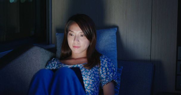Woman watch on tablet and sit on sofa at night - 写真・画像