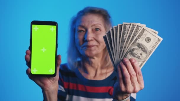 Старуха держит смартфон с зеленым экраном и долларовыми купюрами. Приложение для инвестиций - Кадры, видео