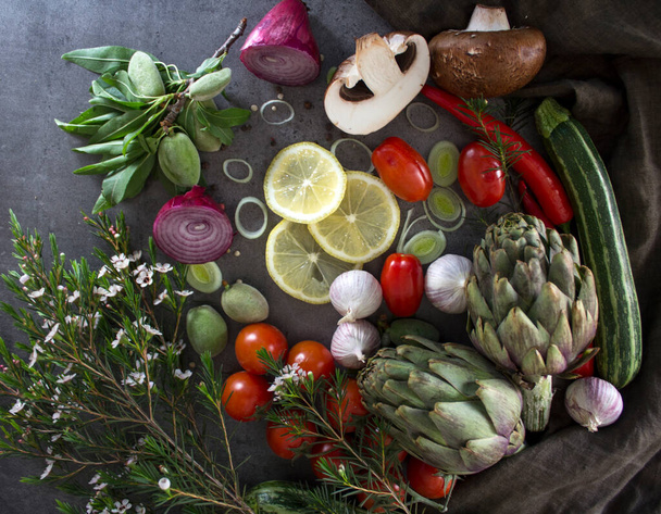 Nyers zöldségek az asztalon. Top view fotó friss articsóka, póréhagyma, cseresznye paradicsom, hagyma, bors, zöld mandula, cukkini, gomba és gyógynövények. Élelmiszer-előkészítő fotó.Egészséges étkezési koncepció. - Fotó, kép