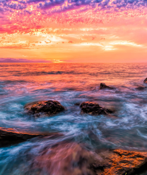 Eine Welle des Sonnenuntergangs bricht am Meeresufer auf, während die Sonne am Ozeanhorizont im vertikalen Bildformat untergeht - Foto, Bild