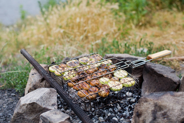 Zöldséges barbecue a tábortűznél a szabadban. Gomba és cukkini fémbélszínből készült rácsban, fogyasztásra kész - Fotó, kép