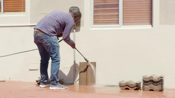 Cleaning tile with water pressure washer. Janitor sprays city street sidewalk paving slabs. Black man disinfects floor and surfaces from coronavirus. Antibacterial sanitary measures on quarantine. - Footage, Video