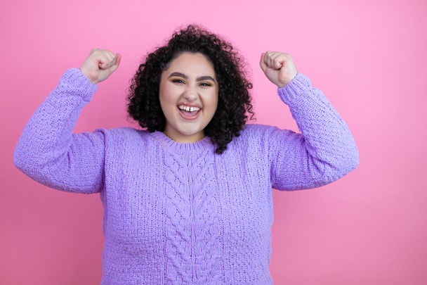 Young beautiful woman wearing casual sweater over isolated pink background very happy and excited making winner gesture with raised arms, smiling and screaming for success. - Photo, Image