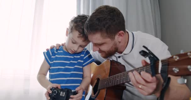 Vater und Sohn spielen Gitarre und fotografieren zu Hause mit der Kamera. - Filmmaterial, Video