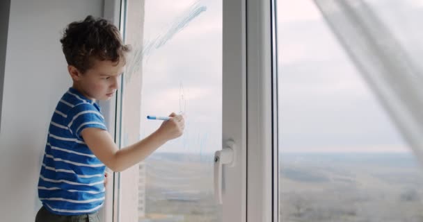 Egy kisfiú rajzol az ablaküvegre egyedül otthon a lakásban.. - Felvétel, videó