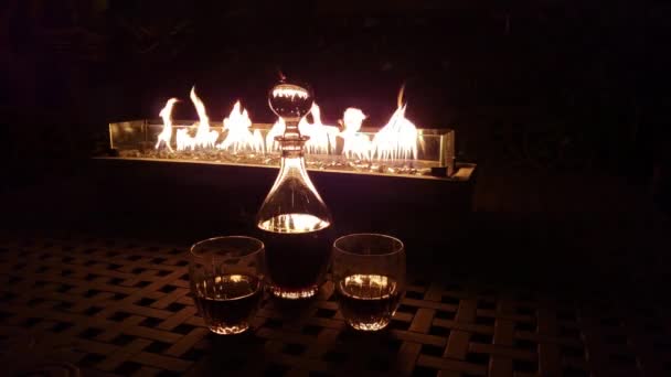 Dekanter i dwie szklanki przed prostokątnym paleniskiem w nocy 4K. - Materiał filmowy, wideo