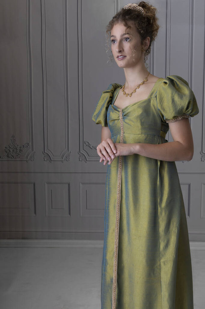 緑の絹のドレスを着て壁に囲まれた部屋に一人で立っている若い摂政女性  - 写真・画像