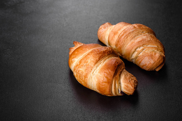 Fresh crisp delicious French croissant with a cup of fragrant coffee on a dark concrete background. Invigorating breakfast - Photo, Image