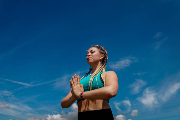 Kaukasische Frau mit Dreadlocks in Meditationshaltung mit dem Himmel im Hintergrund - Foto, Bild
