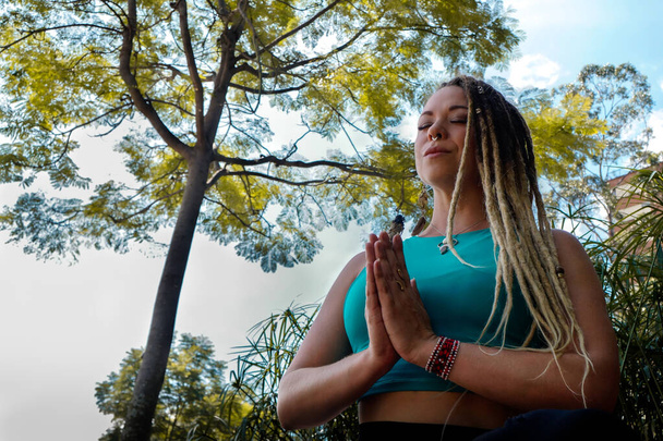 Caucasian woman with dreadlocks in meditation posture under a tree - Photo, Image
