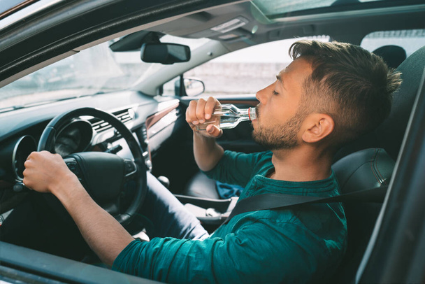 Alkol etkisi altında araba kullanmak. Alkollü araç kullanma. Genç adam elinde bir şişe votka olan bir araba kullanıyor. Sarhoşluk. Tehlikeli sürüş konsepti - Fotoğraf, Görsel