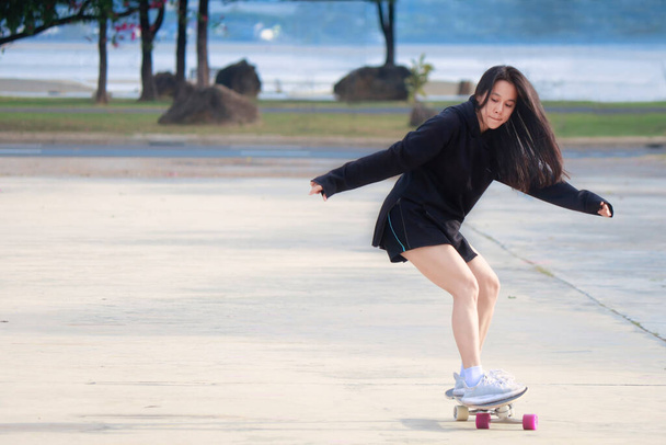 Asiatische Frauen spielen an einem schönen Sommertag im Freien Surfbretter. Fröhliche junge Frauen spielen morgens im Park Surfskate. Lifestylekonzept für sportliche Aktivität. Junge Frauen amüsieren sich mit Surfskate-Board - Foto, Bild