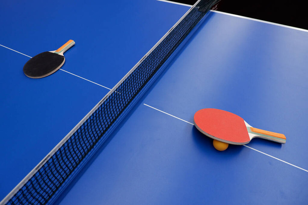 on the tennis table is a ball and two table tennis rackets - Photo, Image
