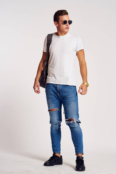 a man with a backpack on his back in jeans t-shirt full length sneakers and glasses on his face - Photo, Image
