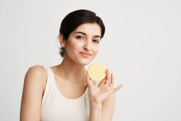 Mujer bonita alegre con una esponja en las manos cuidado de la piel cosméticos color fondo claro - Foto, imagen
