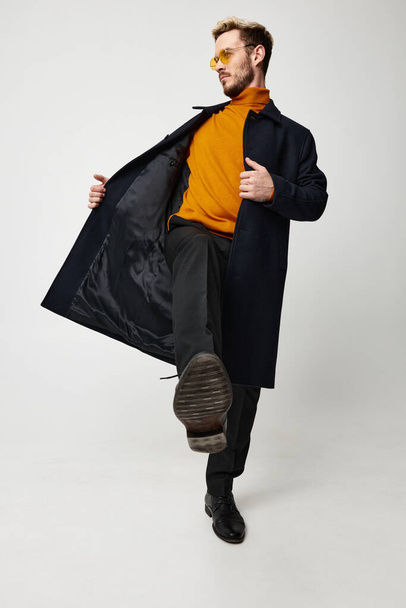 a man in an orange sweater trousers and an unbuttoned jacket is dancing on a light background - Foto, immagini