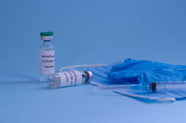 Mavi arka planda koronavirüs aşısı, şırınga, tıbbi maske ve tıbbi eldiven bulunan şişeler..  - Fotoğraf, Görsel