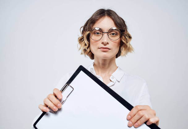 Ділова жінка тримає в руках папку з білим аркушем на макеті світлого фону
 - Фото, зображення