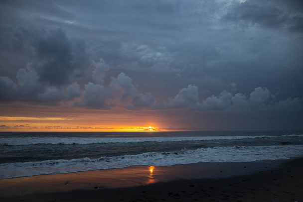 Hihetetlenül gyönyörű naplemente az óceán mellett Balin. A fényes nap lenyugszik a vízben. A nap sugarai a felhők mögül kukucskálnak, és a naplemente gyönyörű tükröződése a vízben. - Fotó, kép