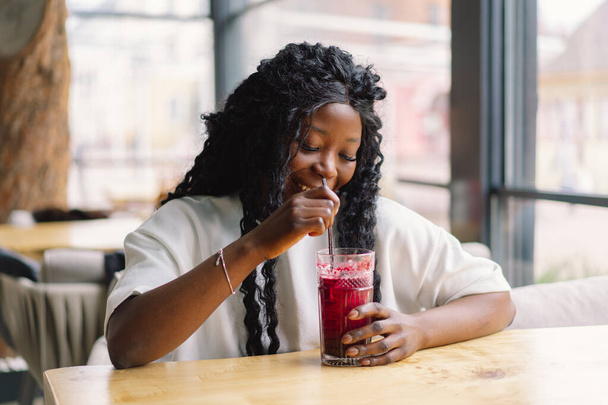 Mujer africana con pelo afro está bebiendo un cóctel. - Foto, Imagen