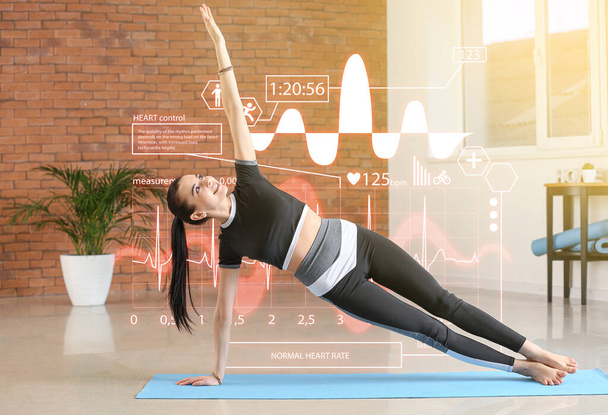 Виртуальный экран монитора сердечного ритма и спортивная молодая женщина практикующая йогу дома - Фото, изображение