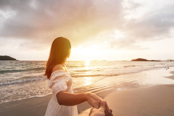 Young woman traveler holding man's hand and looking beautiful sunset on the beach, Couple on vacation in summer concept - Foto, afbeelding