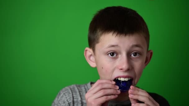 Мальчик на зеленом фоне кладет на тарелку для выравнивания передних верхних зубов, выравнивания верхних зубов. - Кадры, видео