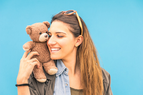Young woman with small vintage teddy bear on her shoulder on a blue wall background - Fotoğraf, Görsel
