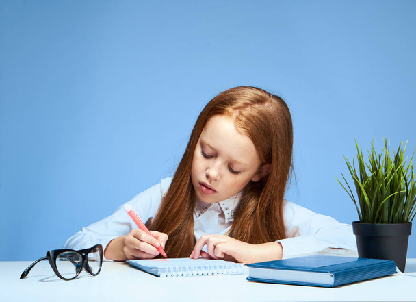 roodharig meisje doet huiswerk aan de tafel schoolvak onderwijs - Foto, afbeelding