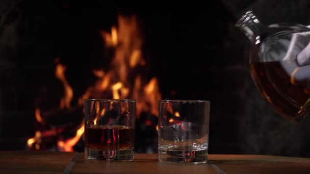 Cognac wordt gegoten uit een fles op de achtergrond van vuur in de open haard - Video
