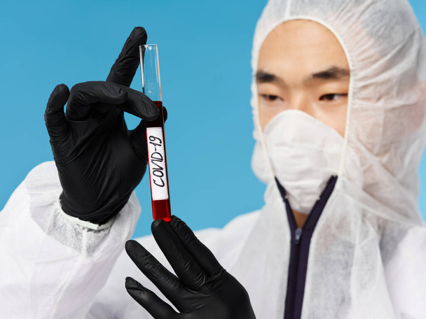man aziatische verschijning beschermende medische pak bloedonderzoek blauw achtergrond - Foto, afbeelding