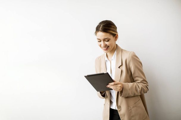 Όμορφη νεαρή γυναίκα κρατά ψηφιακή πλάκα από το λευκό τοίχο στο σύγχρονο γραφείο - Φωτογραφία, εικόνα