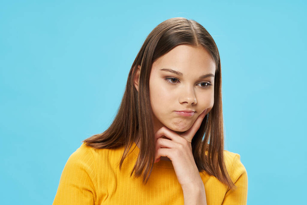 pensive woman in a yellow t-shirt on a blue background touches her face with her hand - Foto, imagen