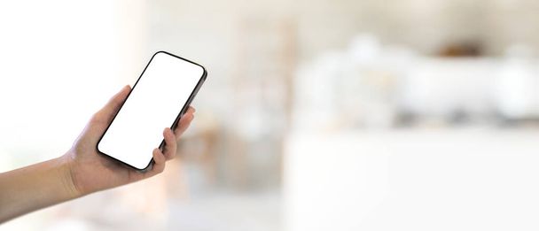 Close up view of female hand holding smartphone with mock up screen in blurred background with copy space, ścieżka wycinania - Zdjęcie, obraz