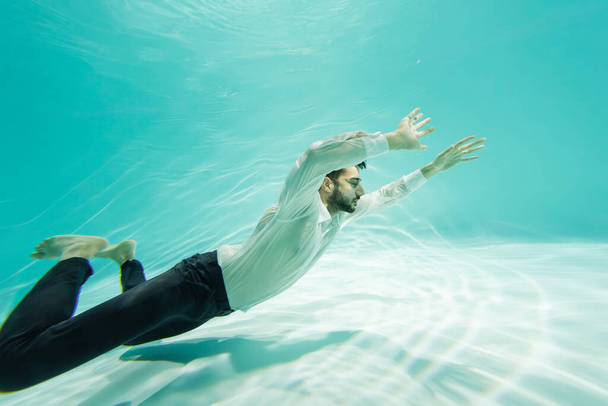 Muslim man in formal wear swimming above bottom in pool  - Valokuva, kuva
