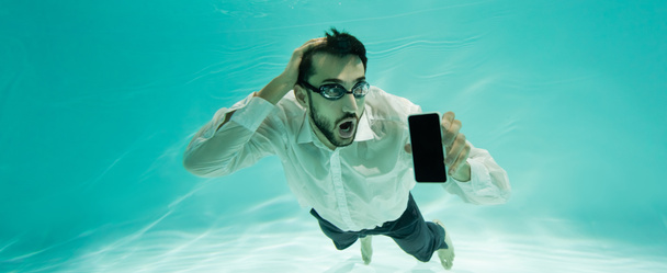 Uomo d'affari musulmano sorpreso che tiene il cellulare mentre nuota in piscina, striscione  - Foto, immagini