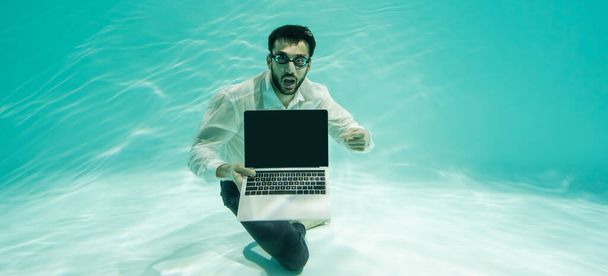 Muslim businessman in goggles pointing at laptop with blank screen in swimming pool, banner  - Photo, Image