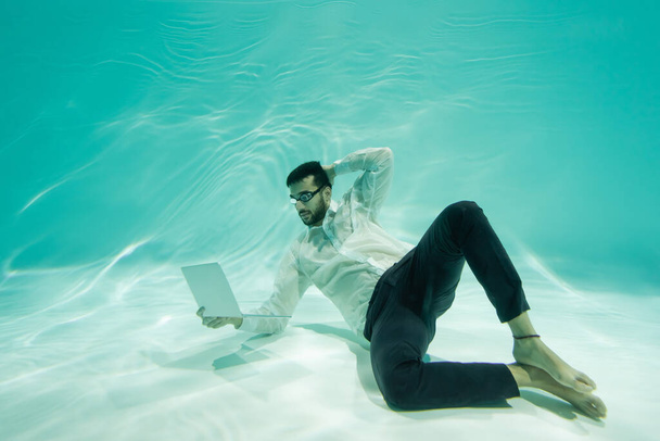 Arabian liikemies katselee kannettavaa tietokonetta uidessaan veden alla  - Valokuva, kuva