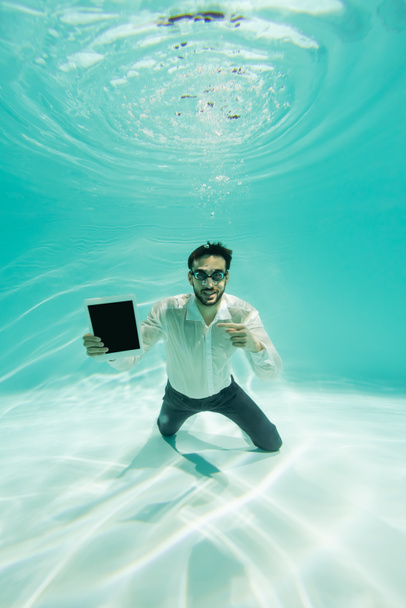Smiling arabian manager pointing at digital tablet underwater  - Photo, Image