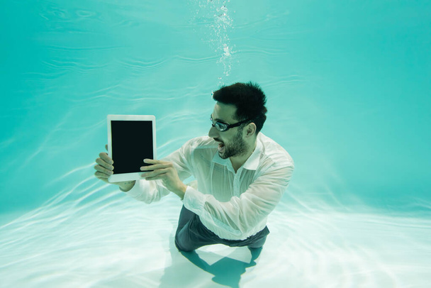 Yüzme havuzunda boş ekranlı dijital tablet tutan neşeli Müslüman iş adamı  - Fotoğraf, Görsel