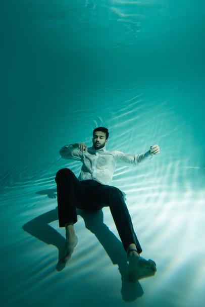 Uomo musulmano in abbigliamento formale nuotare sott'acqua con gli occhi chiusi  - Foto, immagini