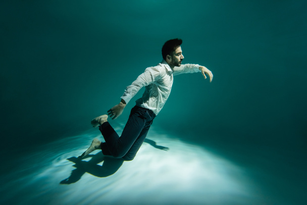 Uomo musulmano in abbigliamento formale nuotare sott'acqua in piscina con ondulazione - Foto, immagini