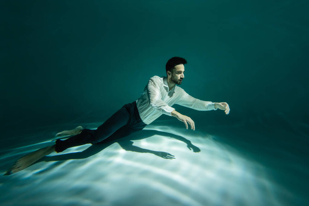 Homem árabe barbudo nadando debaixo d 'água na piscina com luz  - Foto, Imagem