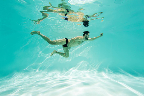 Арабский пловец в очках ныряющий в бассейне с бирюзовой водой  - Фото, изображение