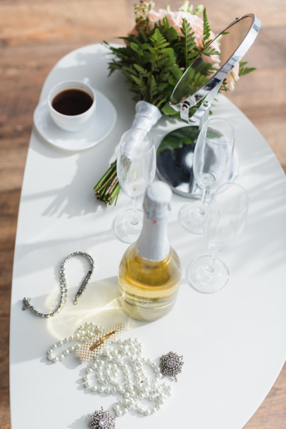 Blick auf Perlenkette, Champagner, Hochzeitsstrauß und Tasse auf Couchtisch - Foto, Bild
