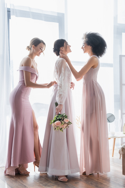 side view of interracial bridesmaids preparing bride for wedding - Photo, Image