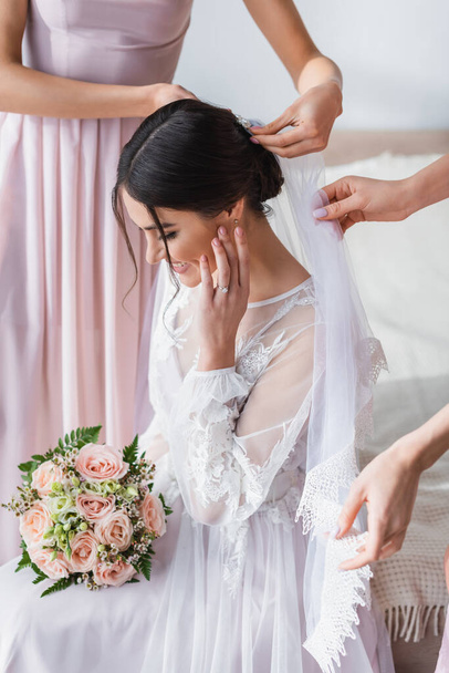 bridesmaids fixing veil of happy bride holding wedding bouquet - 写真・画像