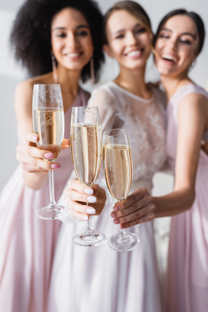 mariée heureuse avec des demoiselles d'honneur interracial tenant des verres de champagne sur fond flou - Photo, image